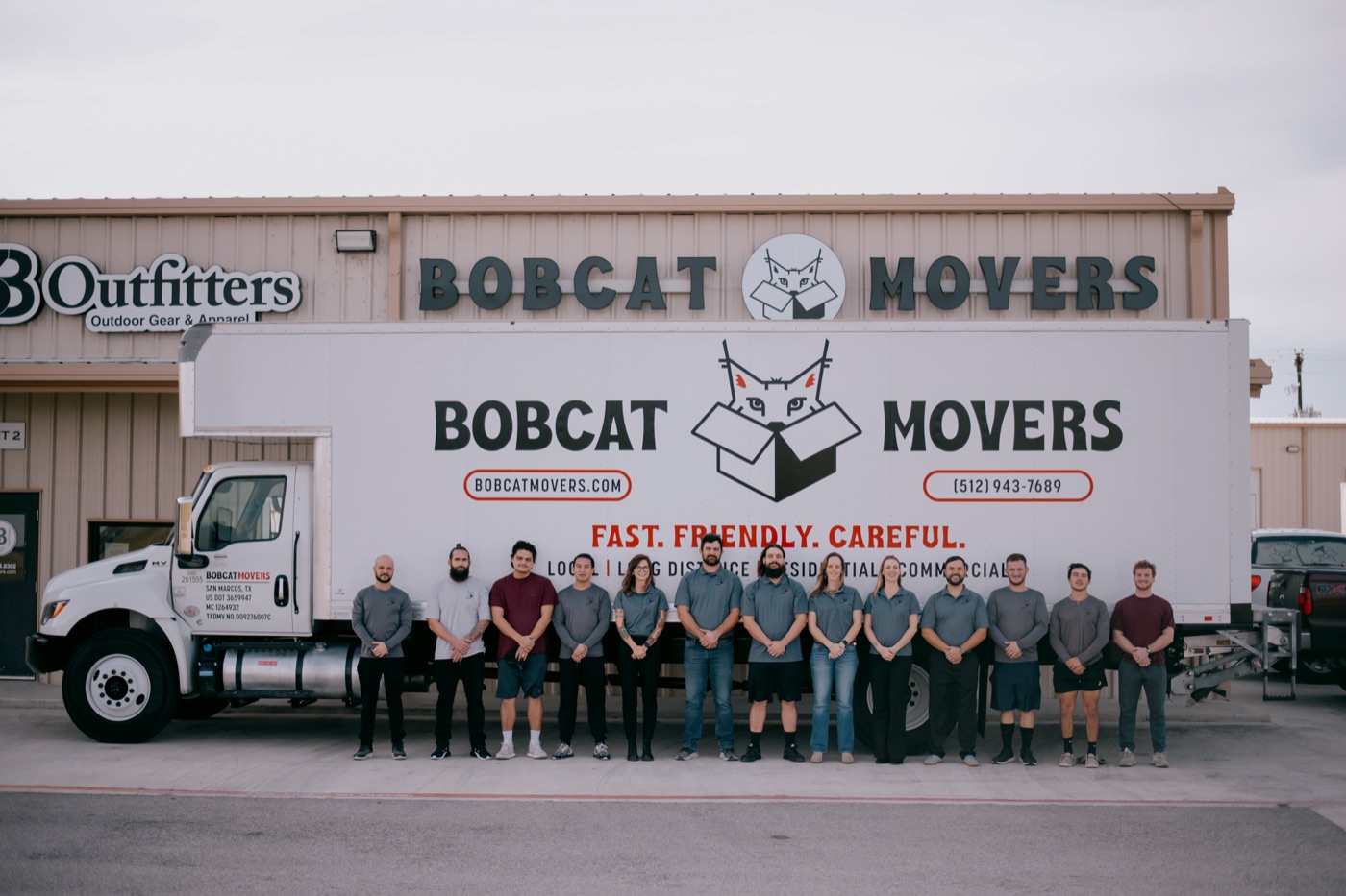 The Bobcat Movers team lined up in front of a Bobcat Movers truck outside the office