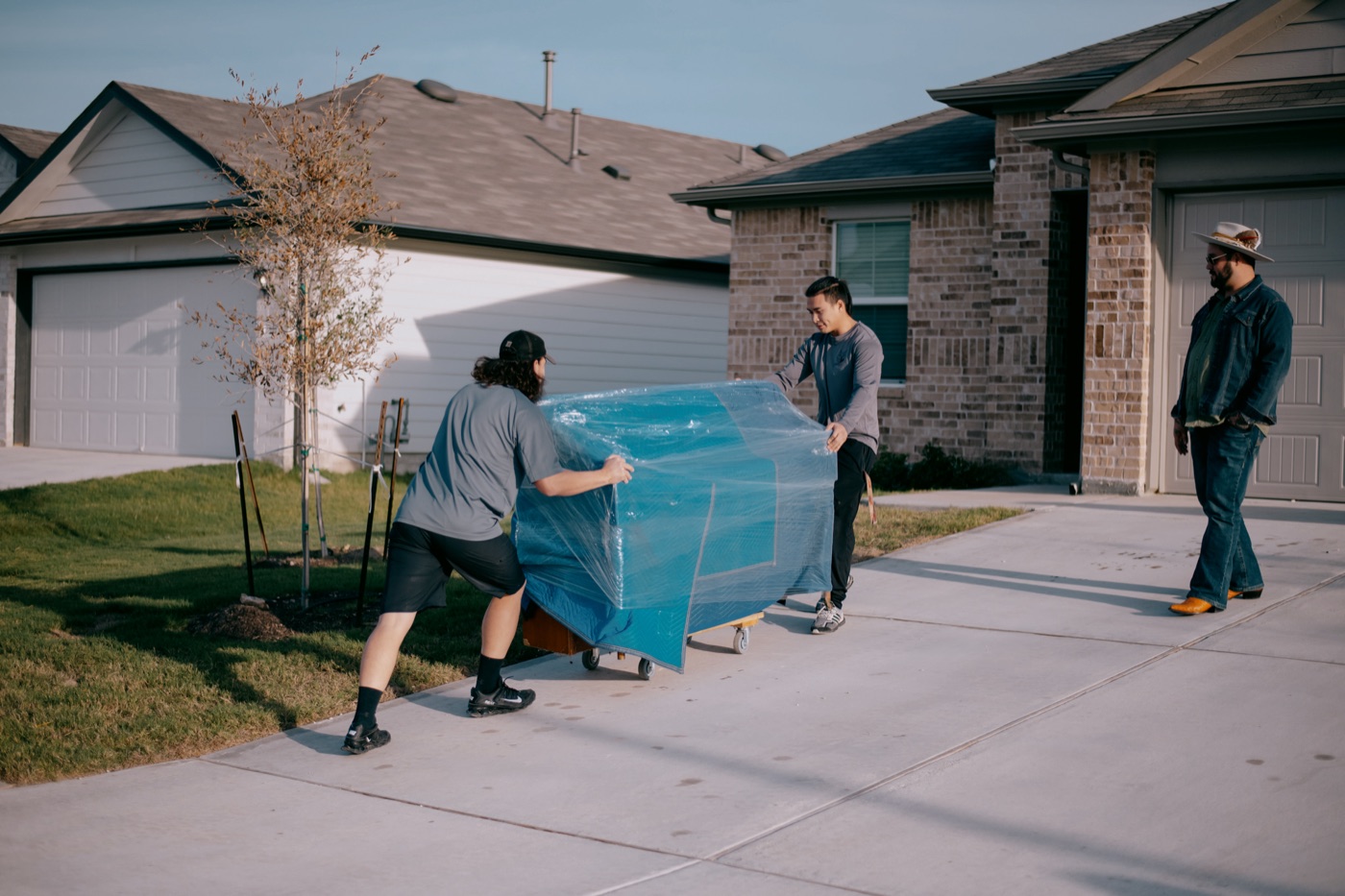 Bobcat Movers crew carrying wrapped furniture down a suburban driveway, the kind of move they do in Pflugerville, TX